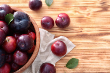 Bowl with ripe juicy plums on wooden table