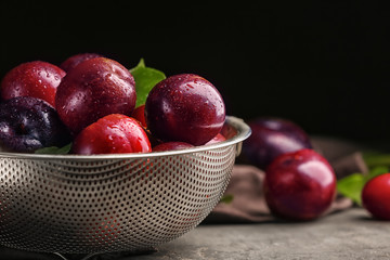 Strainer with ripe juicy plums on dark background
