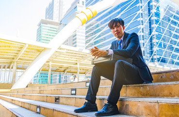 A young Asian businessman in town. A man sitting on staircase. He is unhappy and sad.Portrait, Handsome,Bangkok, Thailand. Photo businessman and depression concept.