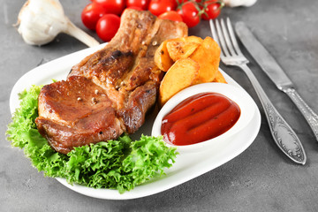 Plate with delicious grilled ribs, vegetables and sauce on table