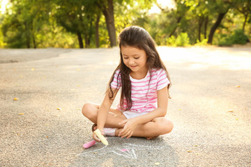 Cute little girl drawing with chalk on asphalt, outdoors