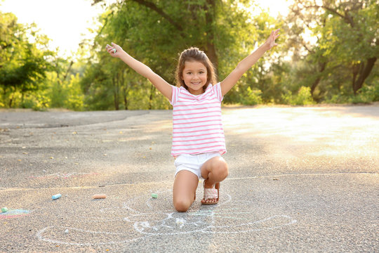 Cute little girl drawing with chalk on asphalt, outdoors