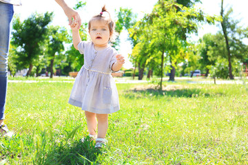 Adorable baby girl holding mother's hand while learning to walk outdoors