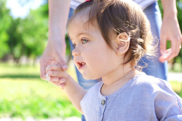 Obraz premium Adorable baby girl holding mother's hand while learning to walk outdoors