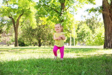 Naklejka premium Cute baby girl learning to walk in park on sunny day