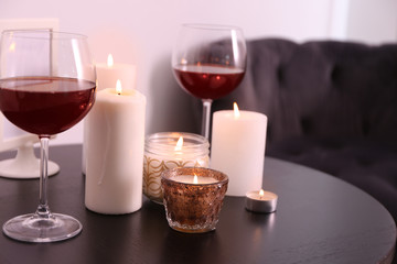 Burning candles and glasses of wine on table in room