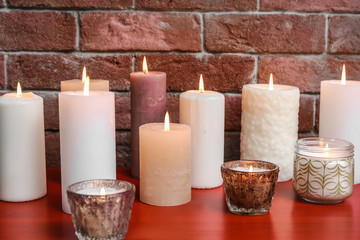 Many burning candles on wooden table against brick wall