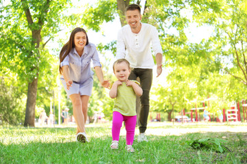 Fototapeta premium Parents supporting their baby daughter while she learning to walk outdoors