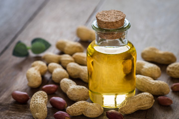 Peanut oil in glass bottle and peanuts on wooden table