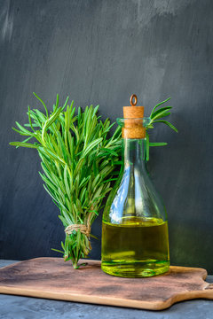 Fresh garden bunch of rosemary with a bottle of rosemary oil or olive oil on cutting board over stone background.