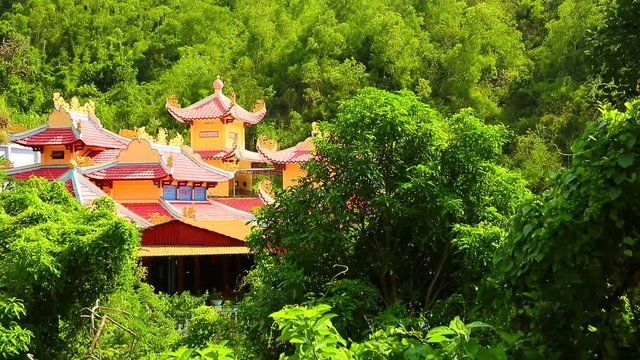 Oriental temple building rooftop nestled on a mountain side, sitting in lush green tropical vegetation, high definition stock footage clip.