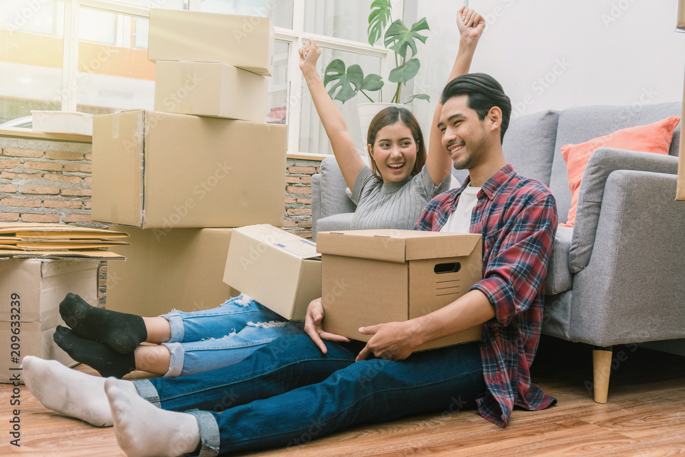 Wall mural asian young couple are glad after successfull packing the big cardboard box for moving in new house,