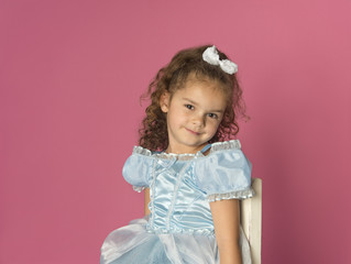 Little girl in blue dress sitting in front of pink background