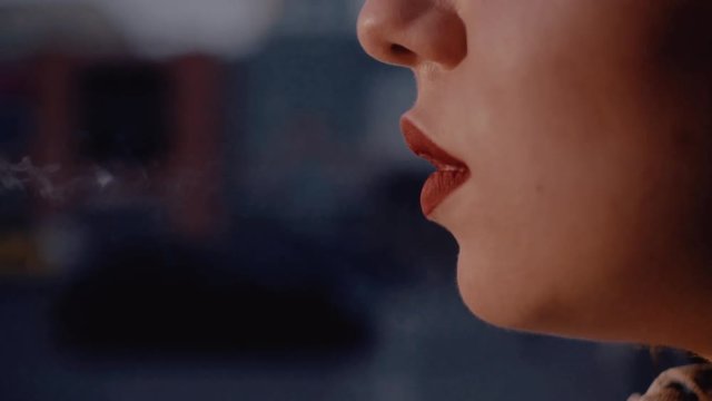 Young attractive Caucasian woman with red lipstick smoking in the street of big city. Lips of young Ukrainian woman. Close-up. Bad habit.