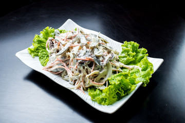 Chinese cuisine, salad with mushrooms, fried beef, pickles, lettuce in a white plate on a black background