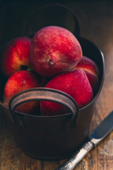 Fresh ripe peaches in a rustic metal container on a wood vintage table top background with a knife