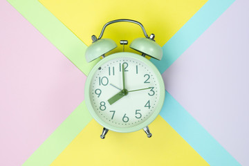 Vintage alarm clock on sweet pastel colored paper top view, background texture, pink, purple, yellow, beige, green and blue colour.