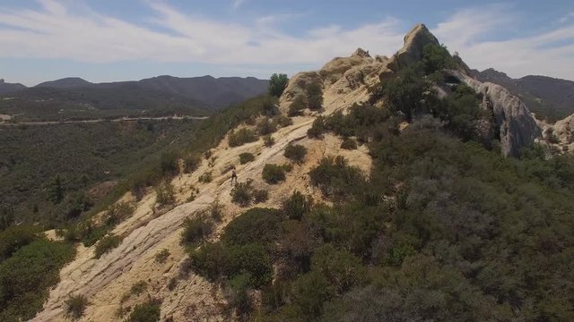 Aerial panoramic view of male jogger making it to the peak of a mountain trail