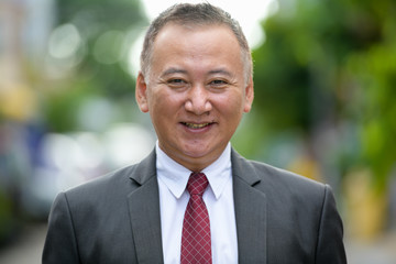 Mature happy Japanese businessman smiling in the streets outdoors © Ranta Images