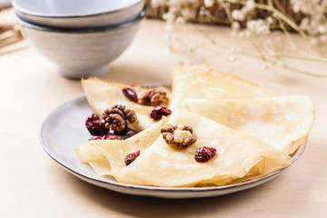 Homemade gluten free rice crepes or pancakes served with dried cranberries and walnuts on wooden table. Healthy breakfast