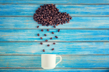 Coffee beans in shape of cloud pouring rain in white cup on blue background