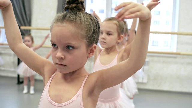 Medium shot of girls of primary school age holding arms in fifth position and practicing ballet moves