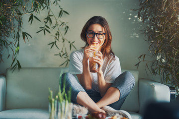 smiling woman drinking healthy fruit infused beverage while relaxing on sofa in trendy restaurant - obrazy, fototapety, plakaty