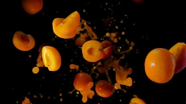 Halves ripe apricots with juice bouncing against to the camera on a black background in slow motion