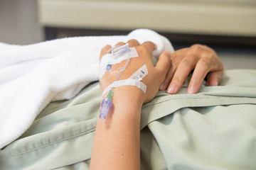 Close up saline drip for patient in hospital room. Patient on the bed.