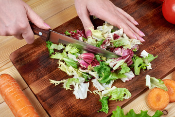 Obraz na płótnie Canvas Female hands chopping green salad , cooking vegetables salad on wooden background