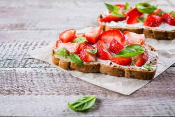 Strawberry bruschetta with cottage cheese,basil and strawberry on baking paper on shabby wooden table background, top view, copy space. Summer Snack Food.