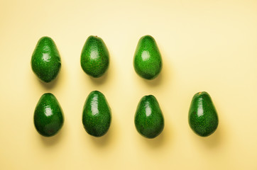 Green avocado pattern on yellow background. Top view. Pop art design, creative summer food concept. Organic avocadoes in minimal flat lay style.