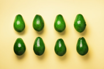 Green avocado pattern on yellow background. Top view. Pop art design, creative summer food concept. Organic avocadoes in minimal flat lay style.
