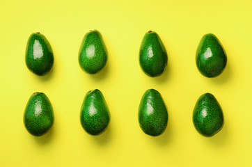 Green avocado pattern on yellow background. Top view. Pop art design, creative summer food concept. Organic avocadoes in minimal flat lay style.