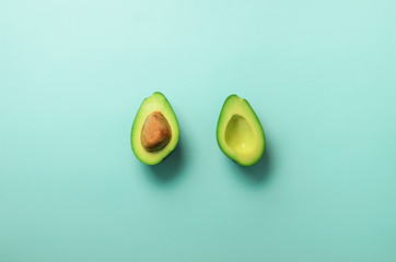 Green avocado halves with seed on blue pastel background. Creative minimal flat lay style with copy space. Summer food concept. Top view. Pop art design.