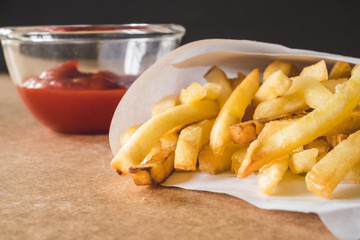 Close up of French fries with ketchup on wooden table.