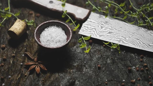 Animation of damascus knife with fresh herbs and spices on wooden table.