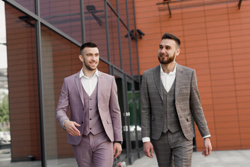 Two smiling young businessmen walking and talking in the city