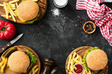 Burgers and french fries on dark stone background, top view with copy space. Homemade hamburgers and fries. Fast food or BBQ concept