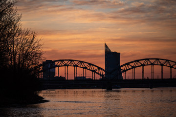 railroad metal bridge silhouette over river of Daugava in Riga, Latvia in dark red sunet