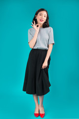 Full body of smiling asian woman dressed in pin-up style dress over blue.