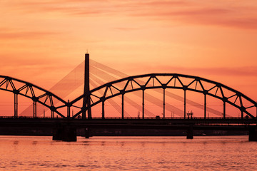 Naklejka na ściany i meble railroad metal bridge silhouette over river of Daugava in Riga, Latvia in dark red sunet