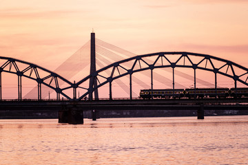 railroad metal bridge silhouette over river of Daugava in Riga, Latvia in dark red sunet