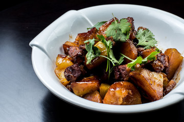 Chinese beef stew with young potatoes in sweet sauce, in white plate on black background