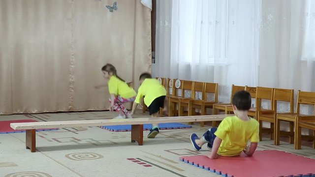 Children in yellow T-shirts make somersaults on tatami and jumping through the bench