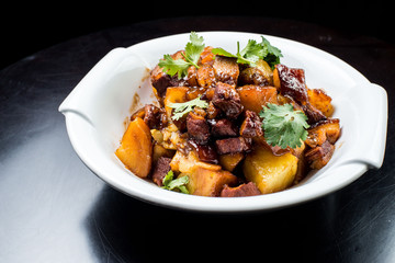 Chinese beef stew with young potatoes in sweet sauce, in white plate on black background