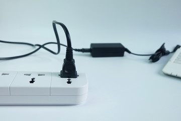 Close up plug in Adapter power cord charger with blurred laptop computer on white background