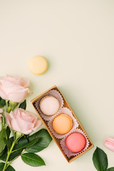 Colorful macaroons and rose flowers on light green. Sweet macarons in gift box. Top view