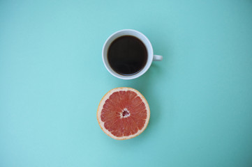 A cup of coffee on and a half of grapefruit on blue.
