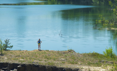 A little woman stands on the shore of a very large and beautiful lake with clear water, Summer trips and tourism, sunny day